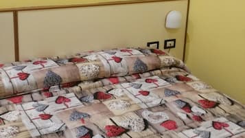 A bed with a patterned bedspread, a wall-mounted picture of a red car, and a bedside lamp.