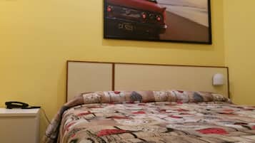 Una camera da letto con una coperta dal disegno vivace, un quadro appeso al muro raffigurante un'auto e un telefono sul comodino.