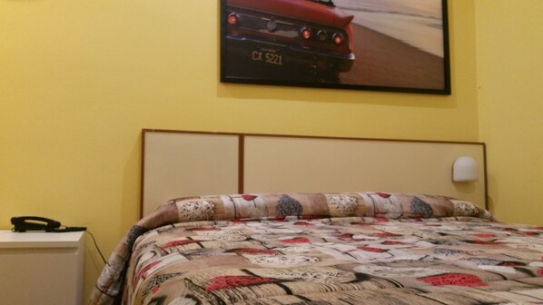 Un dormitorio con una colcha estampada, un cuadro de un coche en la pared y un teléfono en la mesita de noche.