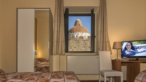 Habitación de hotel con cama, escritorio, silla, televisor y ventana con vista a un edificio histórico.