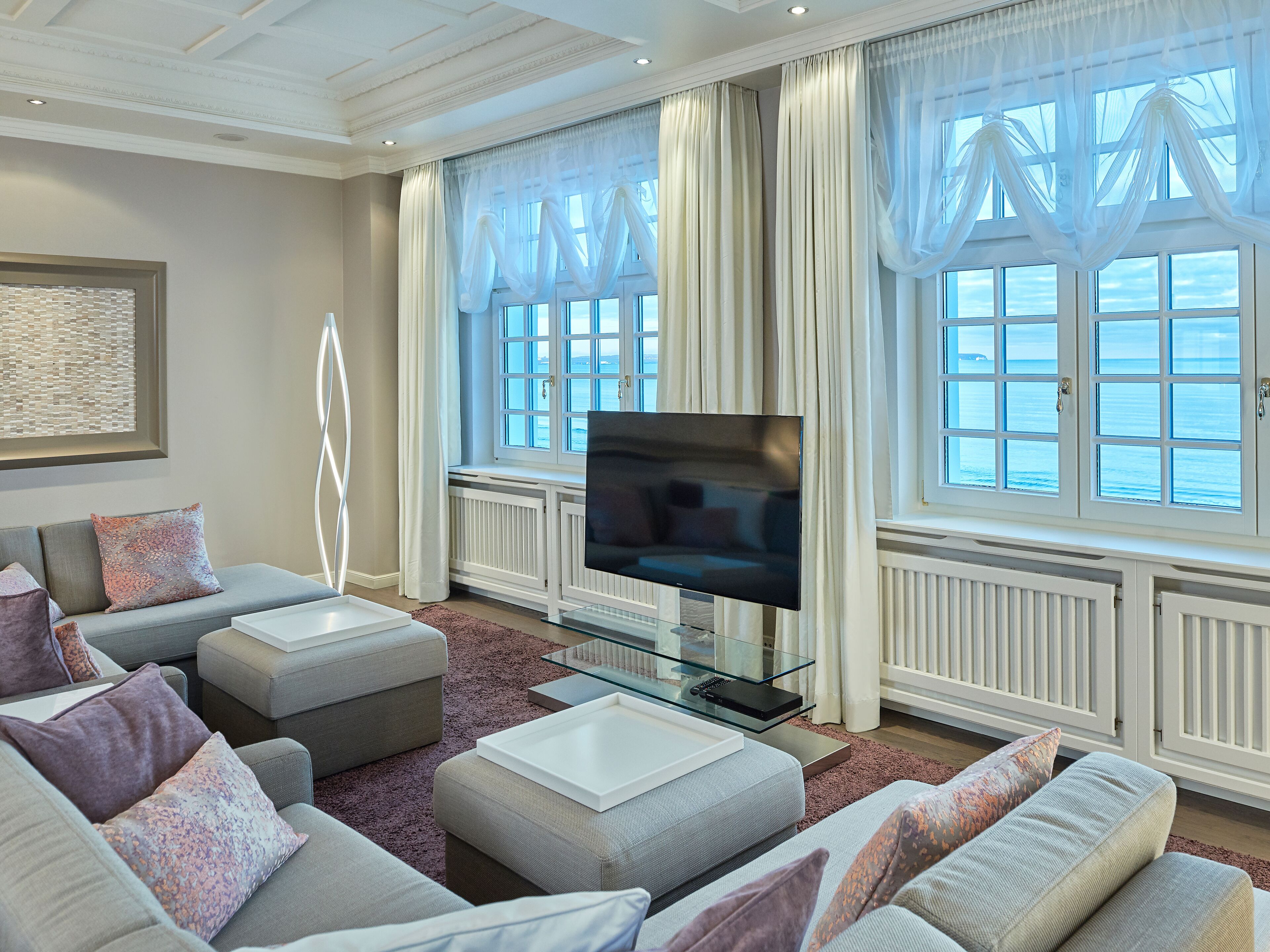 A modern living room with a large flat-screen TV, grey sofas, and a glass coffee table.