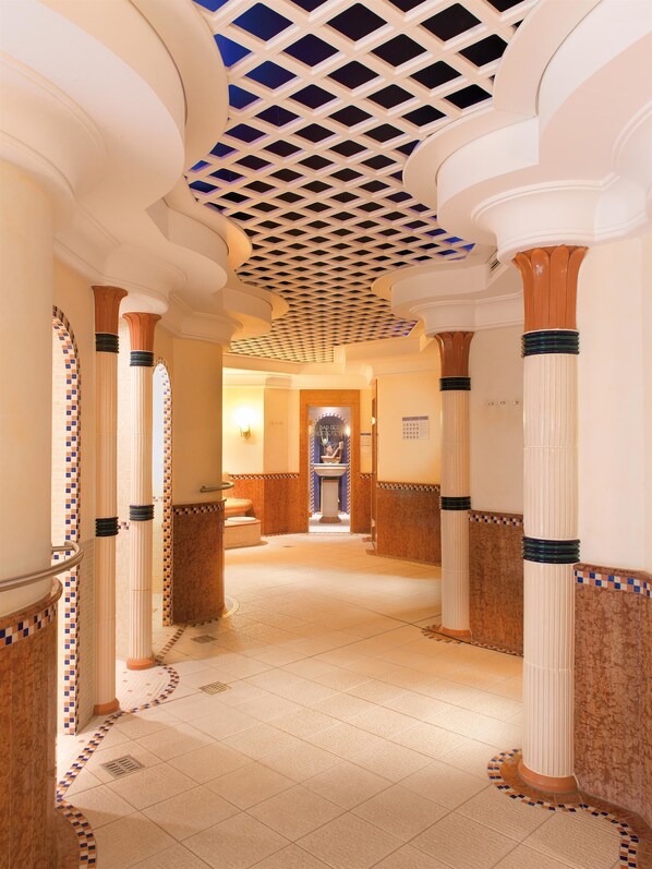 Un pasillo con columnas, baldosas estampadas y un techo decorativo.