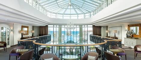 Un hall d’entrée spacieux avec une haute verrière, une table ronde centrale et des espaces aménagés pour s’asseoir.