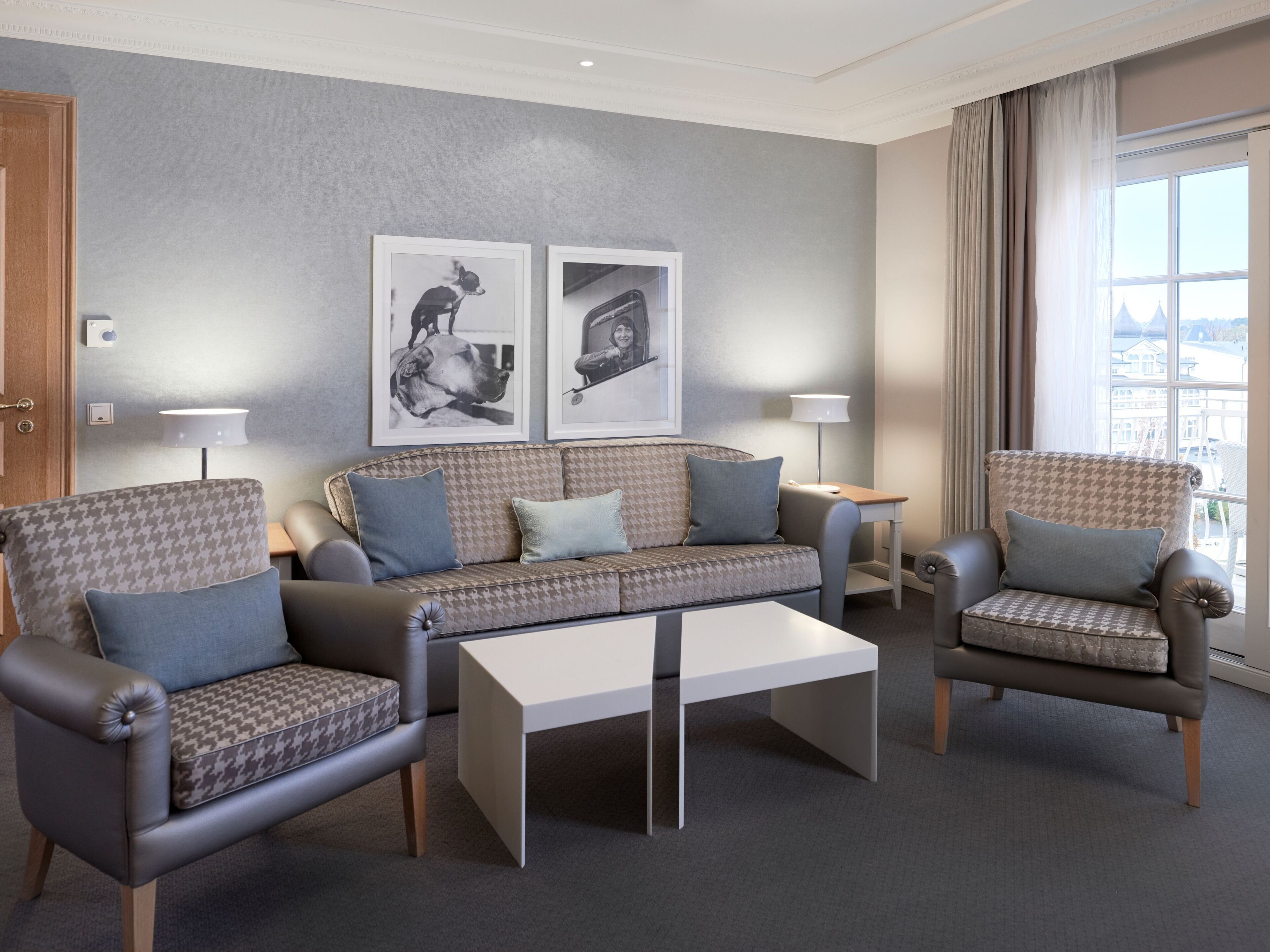 A modern living room with a sofa, two armchairs, a coffee table, and two wall-mounted lamps. There are two framed pictures on the wall.