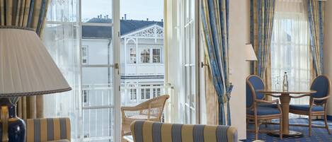A hotel room with a balcony, striped armchairs, a dining table, and a view of a building.
