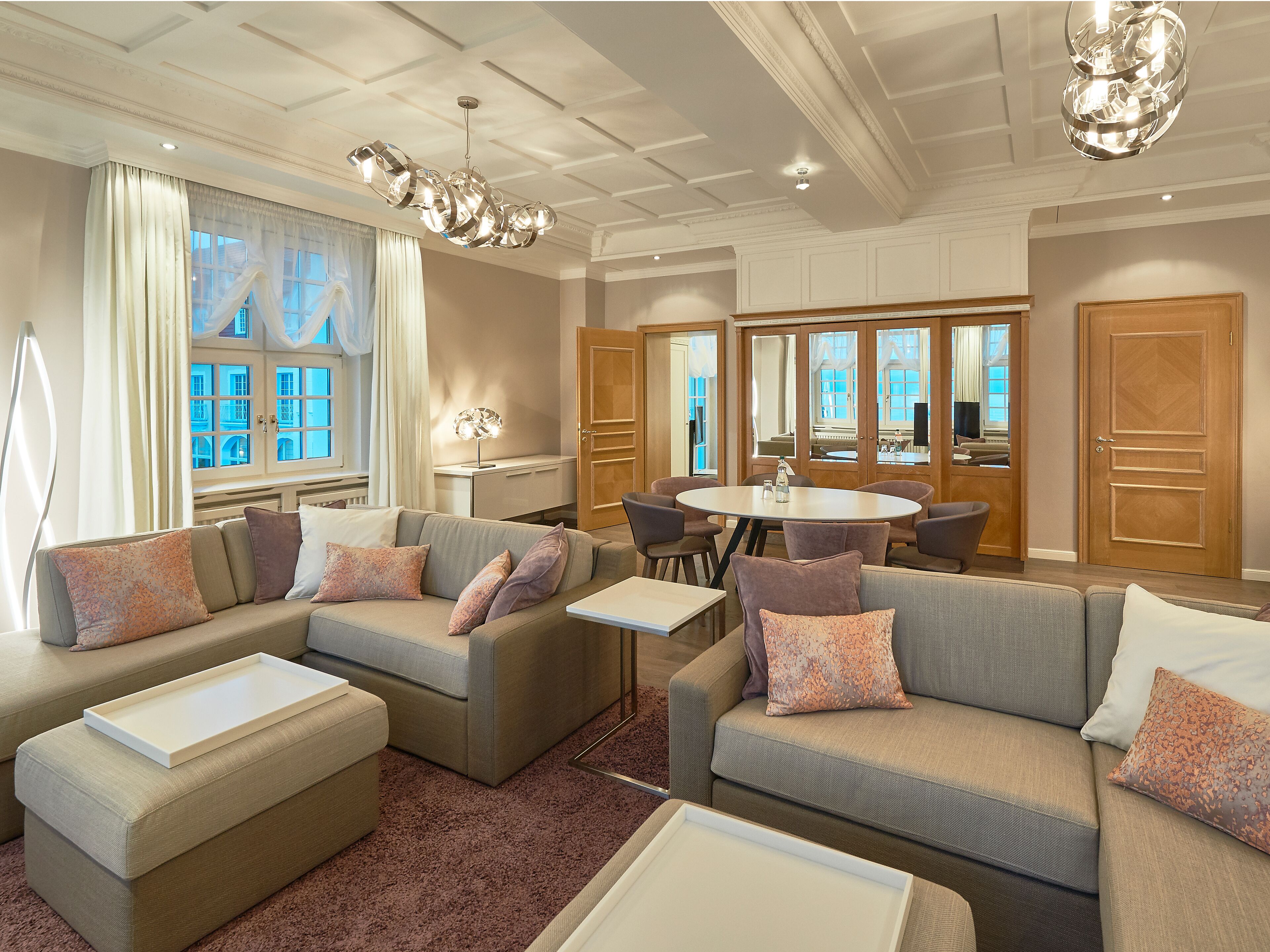 A spacious living room with a large sofa set, a dining table, and a chandelier.