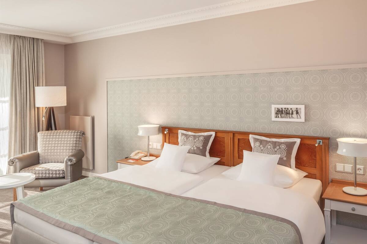 A hotel room with a large bed, two bedside tables, a chair, a lamp, and a patterned wall.