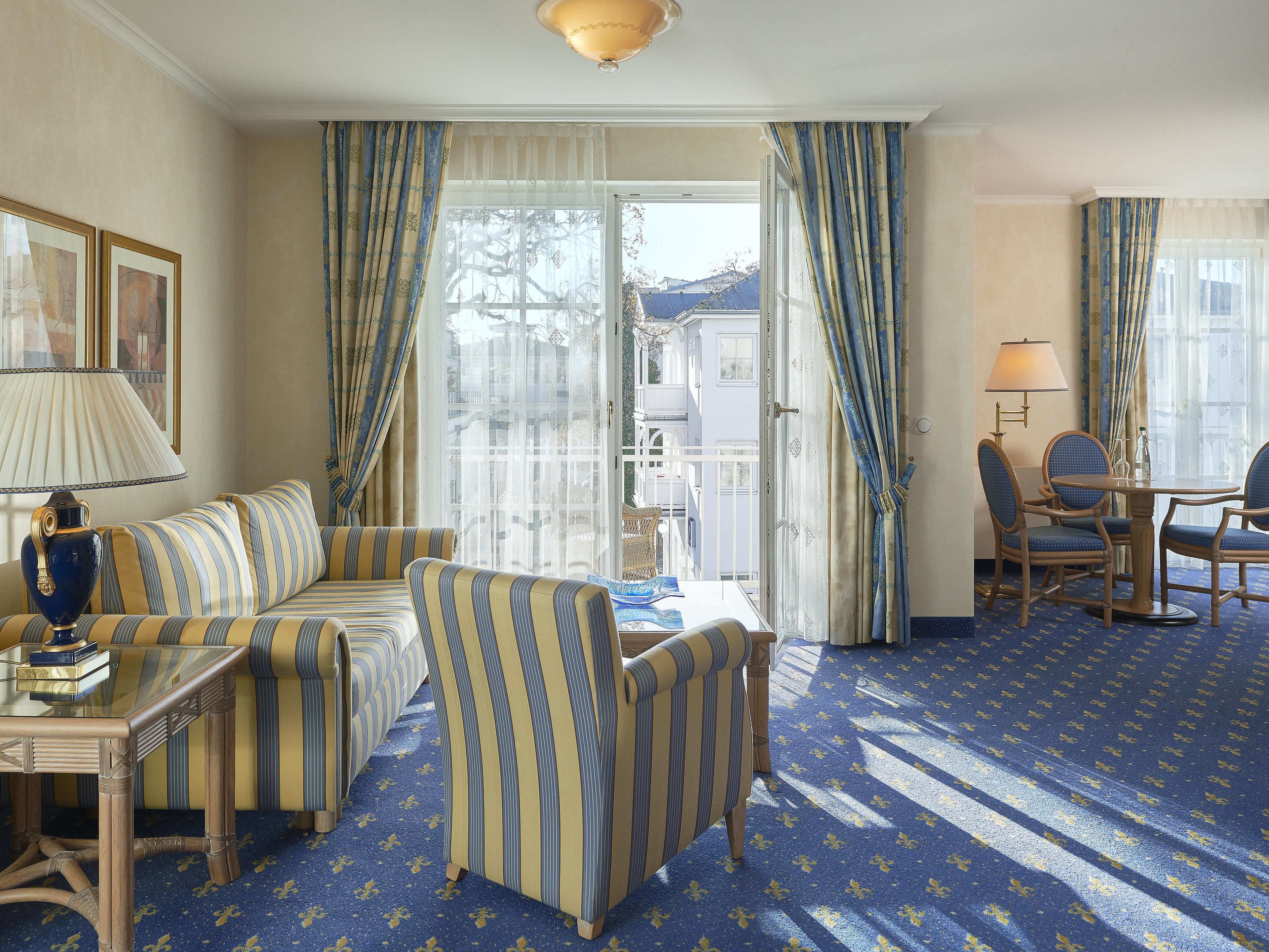 A hotel room with a sofa, chairs, a small table, and a view of the outside.