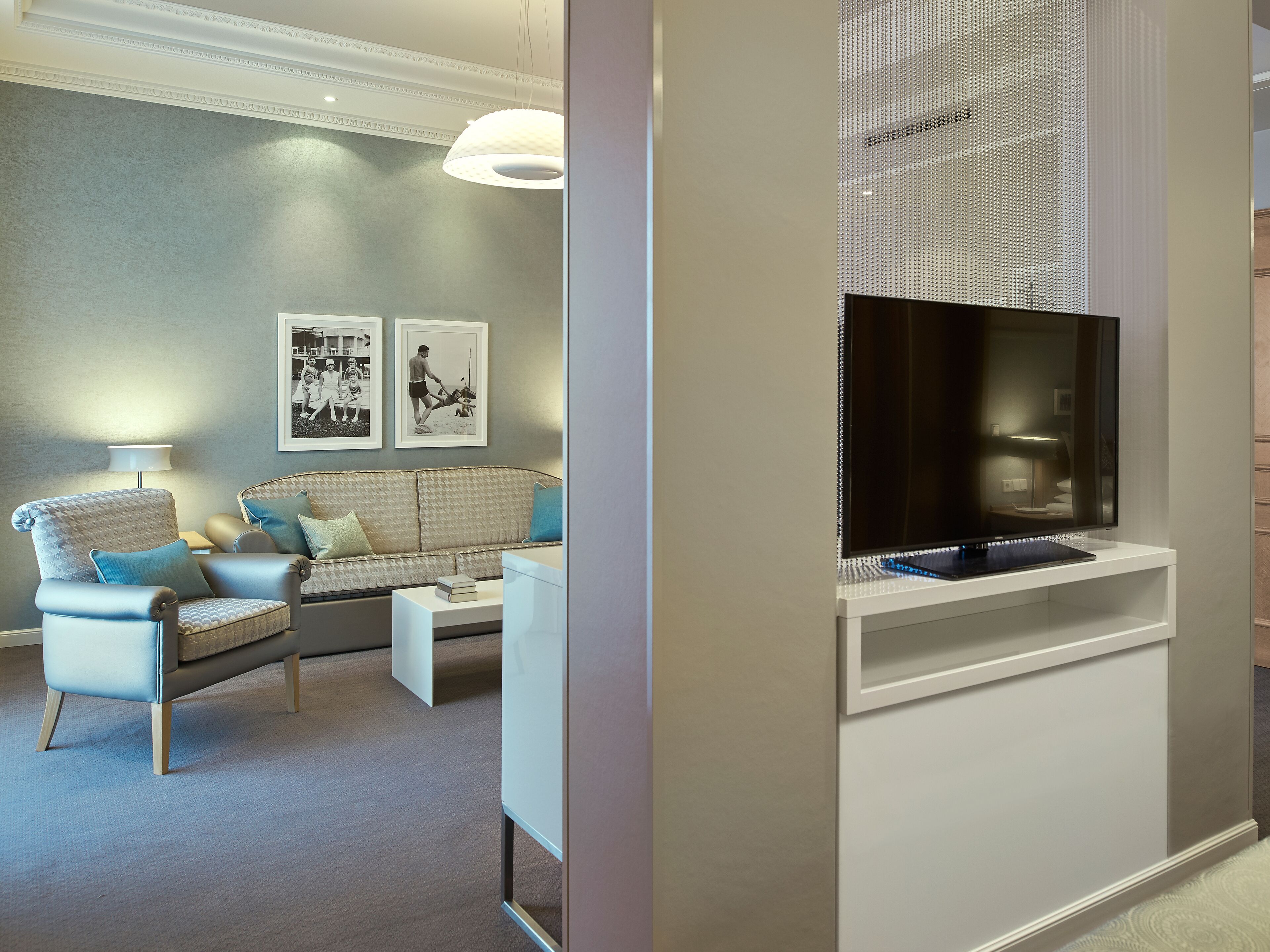 Ein modernes Wohnzimmer mit einer Couch, Sesseln, einem Flachbildfernseher und gerahmten Bildern an der Wand.