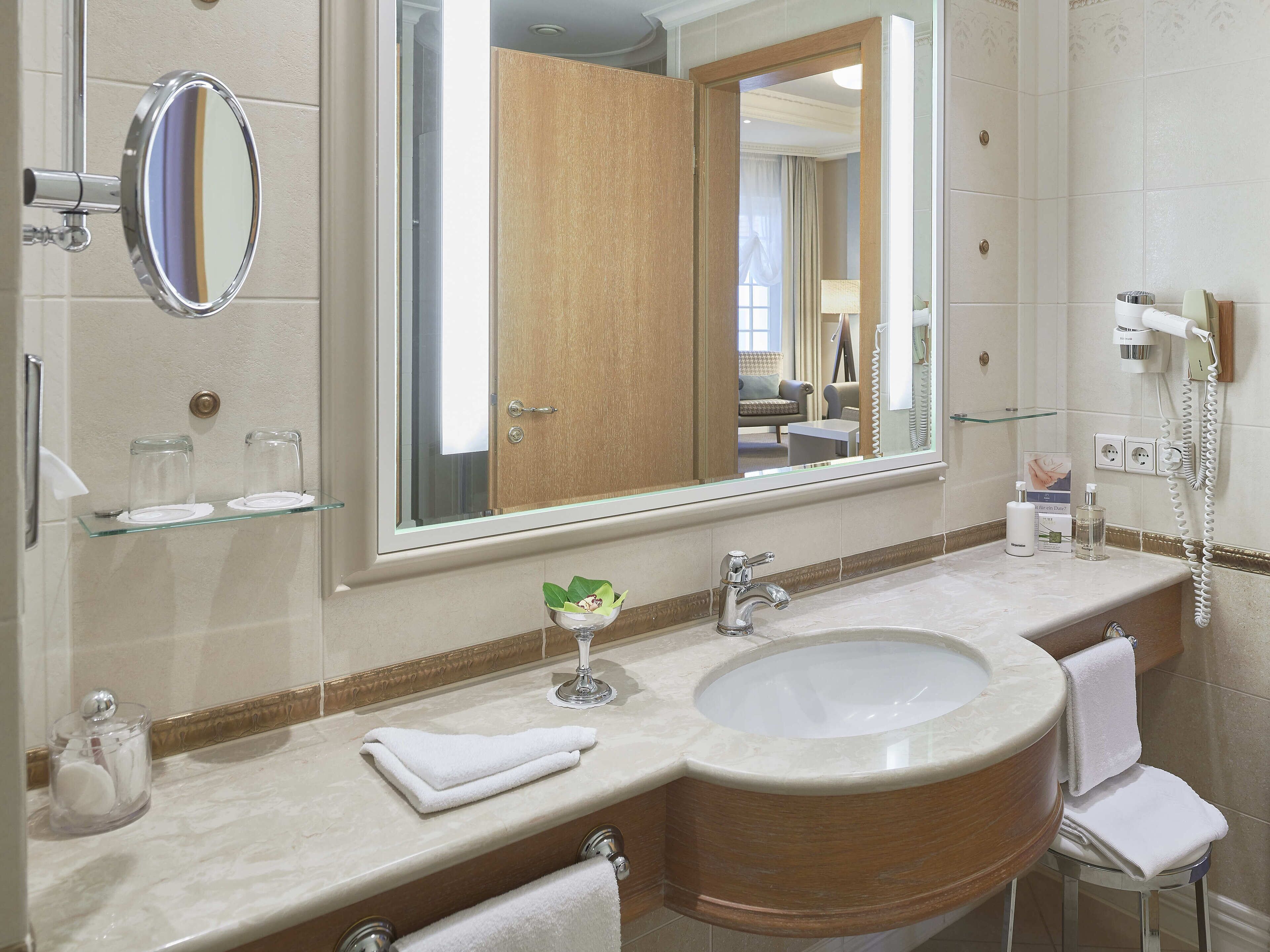 A bathroom with a large mirror, two sinks, a vanity, and a towel rack.