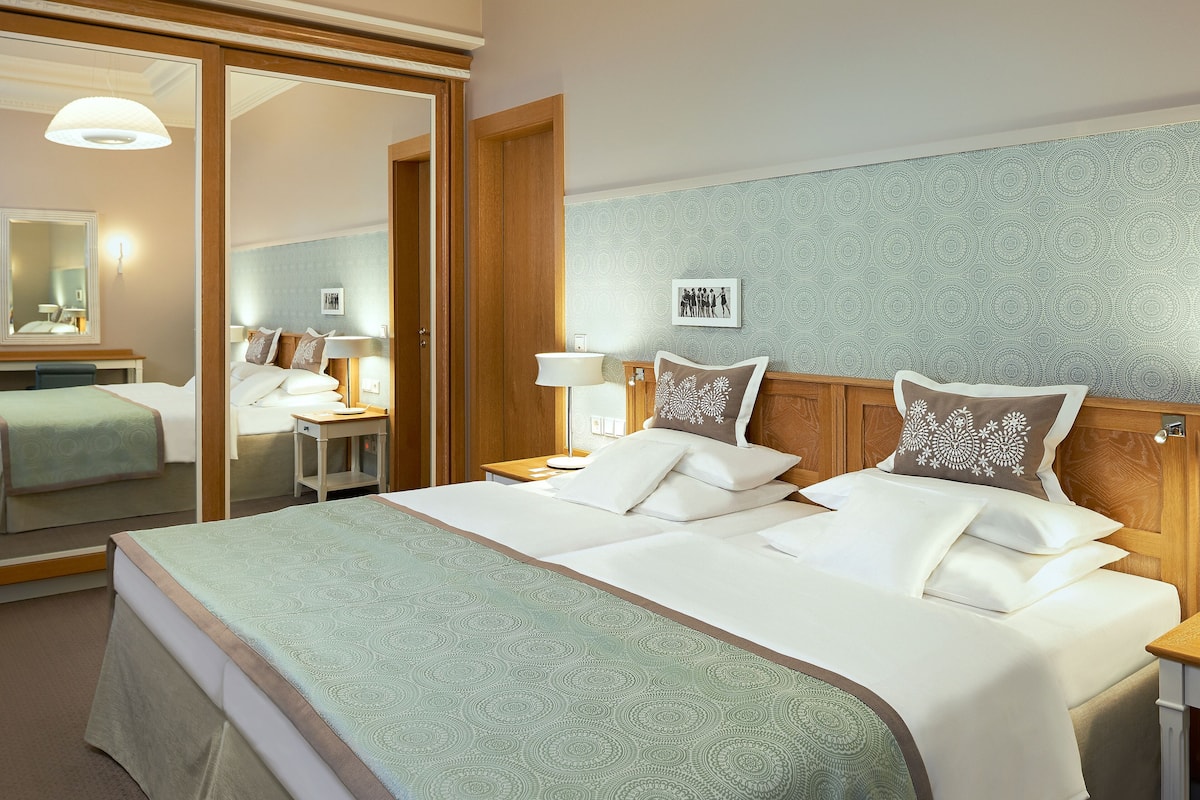 A hotel room with a large bed, a bedside table, a mirror, and a wardrobe.