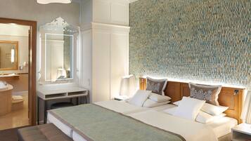 Habitación de hotel con una cama grande, una mesita de noche, un espejo, un baño con lavamanos e inodoro, y una pared con diseño.