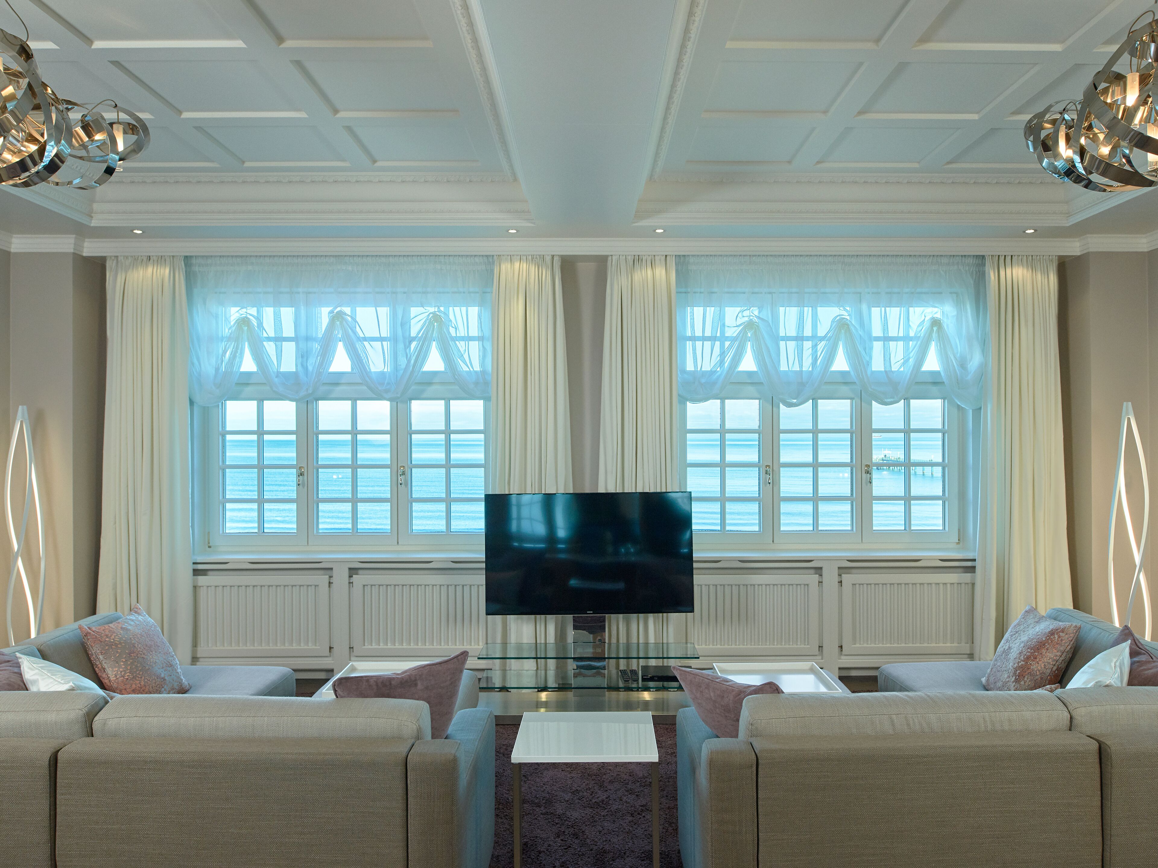A spacious living room with a large flat-screen TV, comfortable seating, and large windows with curtains.