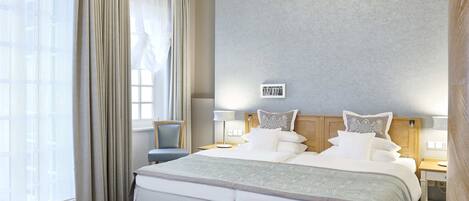 A hotel room with a large bed, a chair, a bedside table, and a window with curtains.