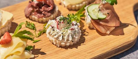 Une planche en bois sur laquelle sont disposés divers aliments, notamment un sandwich à la fraise, un morceau de fromage et une amuse-gueule à base de viande.