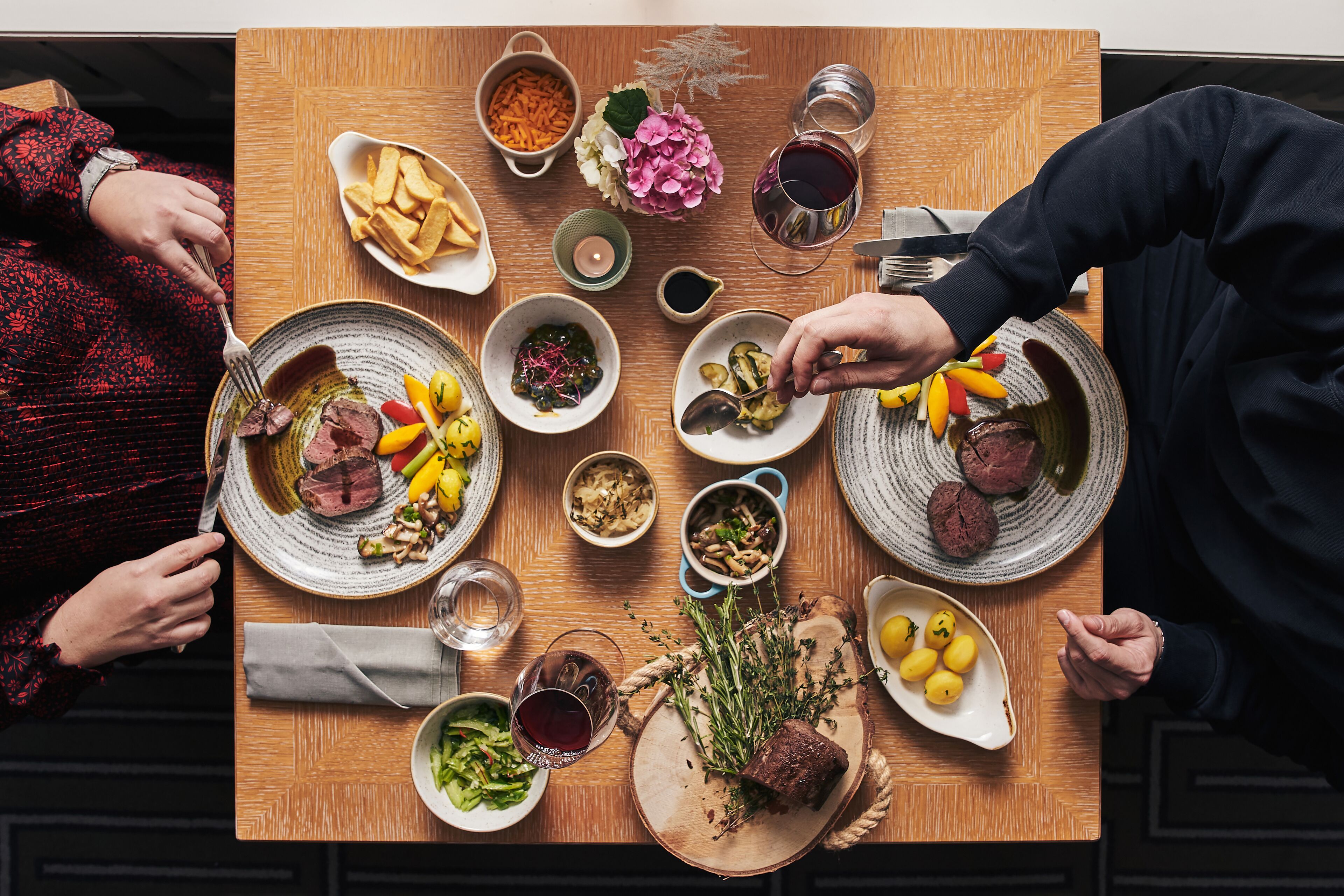 A dining table with various dishes, including meat, vegetables, and a bottle of wine.