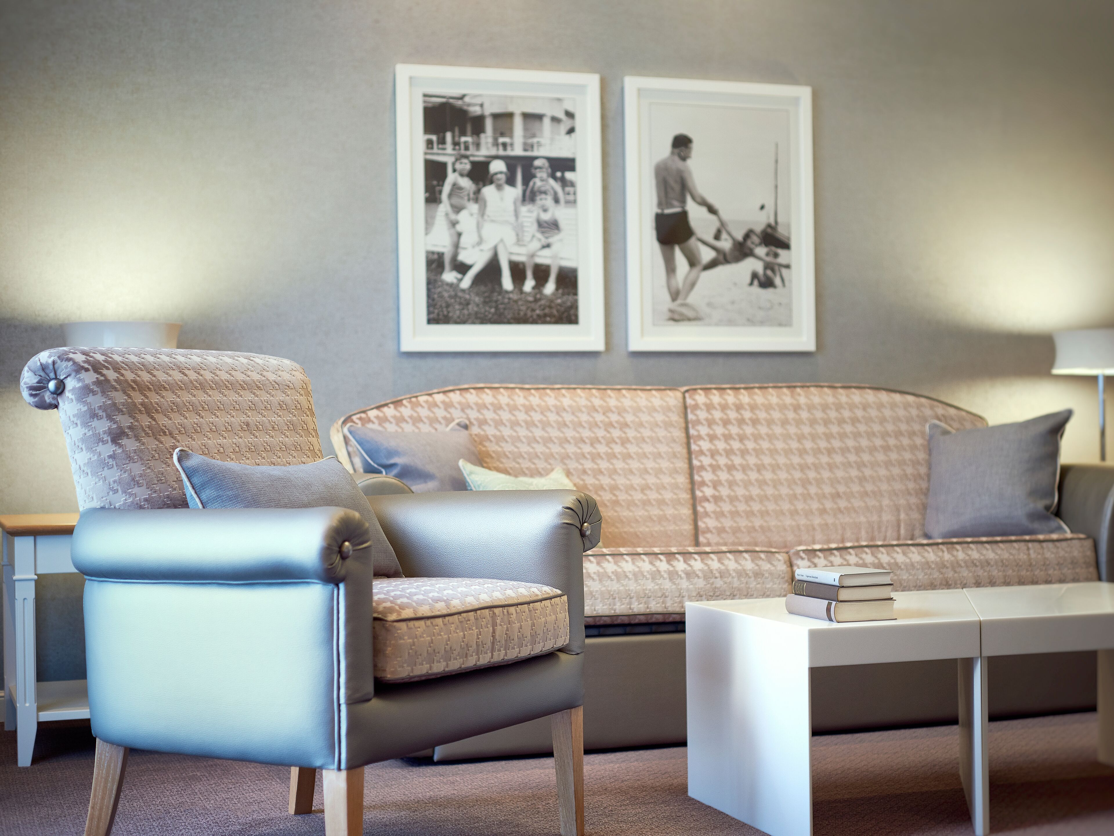 A modern living room with a grey sofa, a blue armchair, and a white coffee table. There are two framed black and white photographs on the wall.