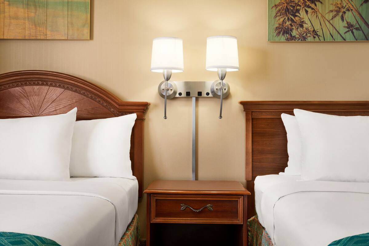 A hotel room with two beds, a nightstand with a drawer, and two wall-mounted lamps.