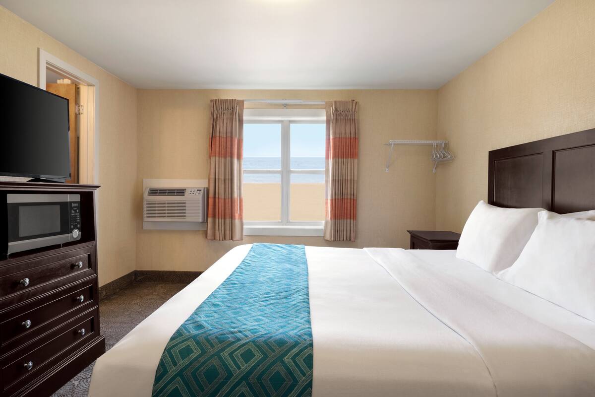 A hotel room with a bed, a TV, a dresser, an air conditioner, and a window with curtains.