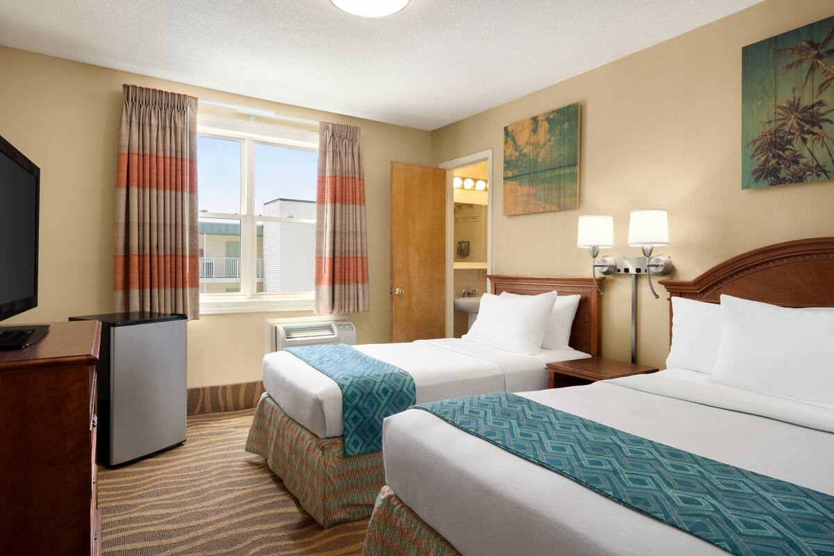 A hotel room with two beds, a desk with a refrigerator, a television, and a window with curtains.
