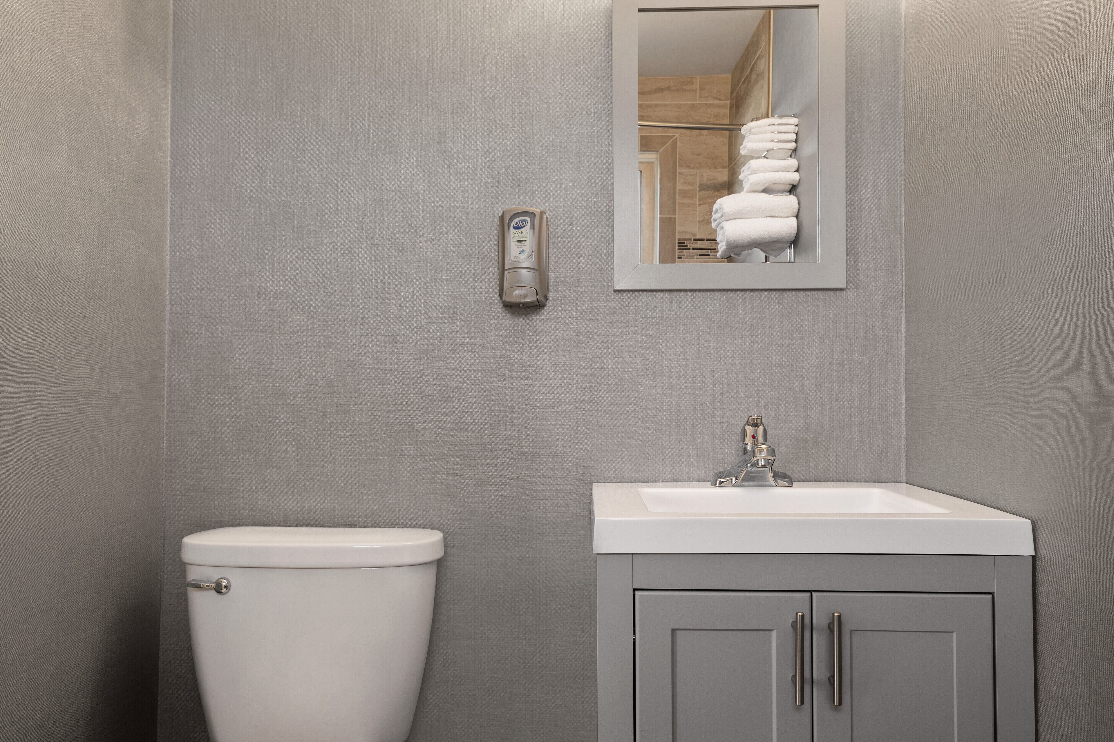 A modern bathroom with a toilet, sink, and a towel dispenser.