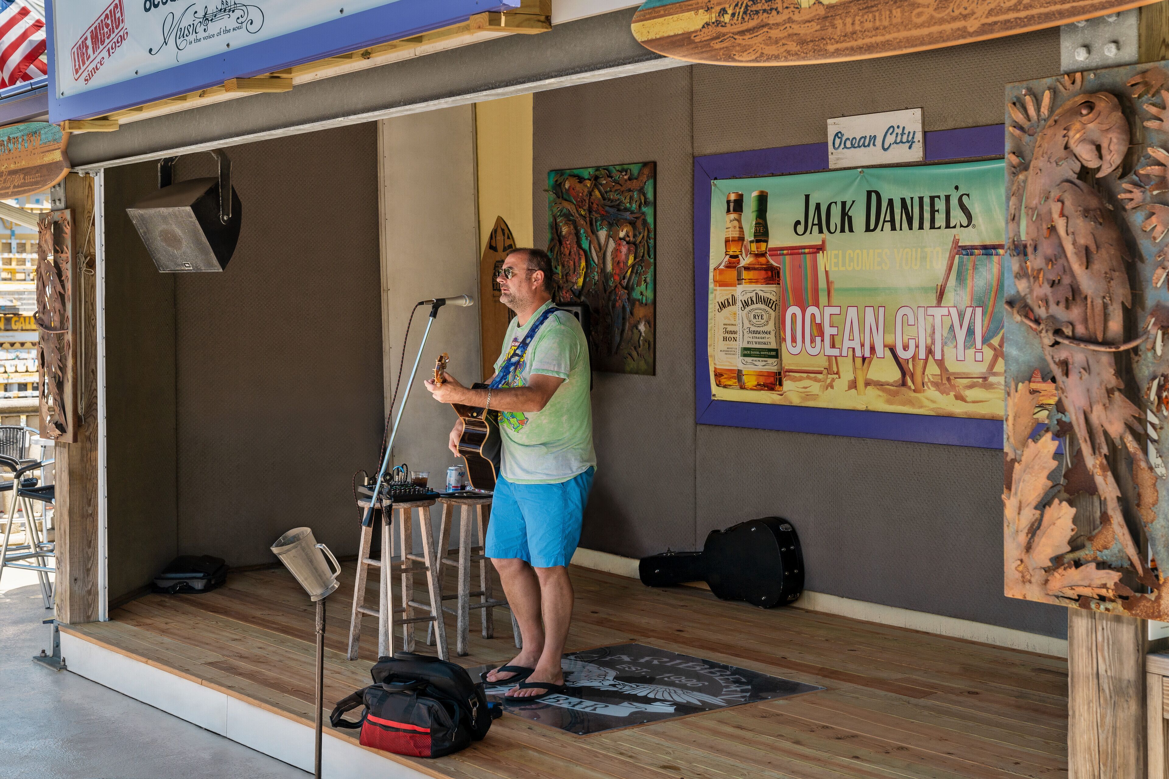 A musician performing on a stage with a microphone stand, a guitar, and a promotional poster for Jack Daniel's.