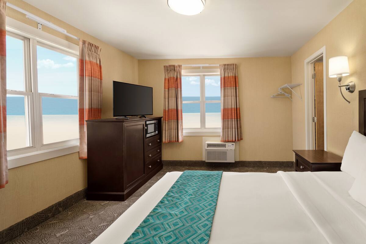 A hotel room with a bed, a TV, a dresser, and a window with curtains.