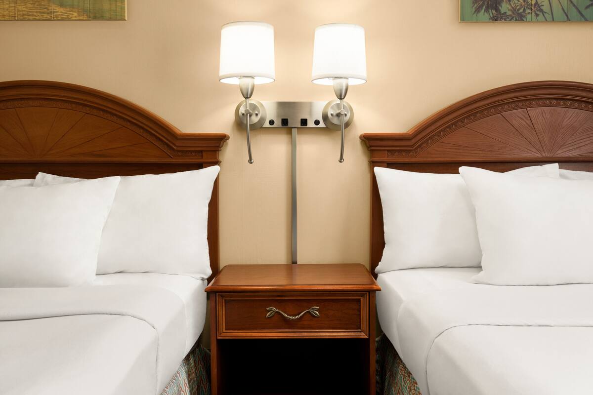 A hotel room with two beds, a nightstand with a drawer, and two wall-mounted lamps.