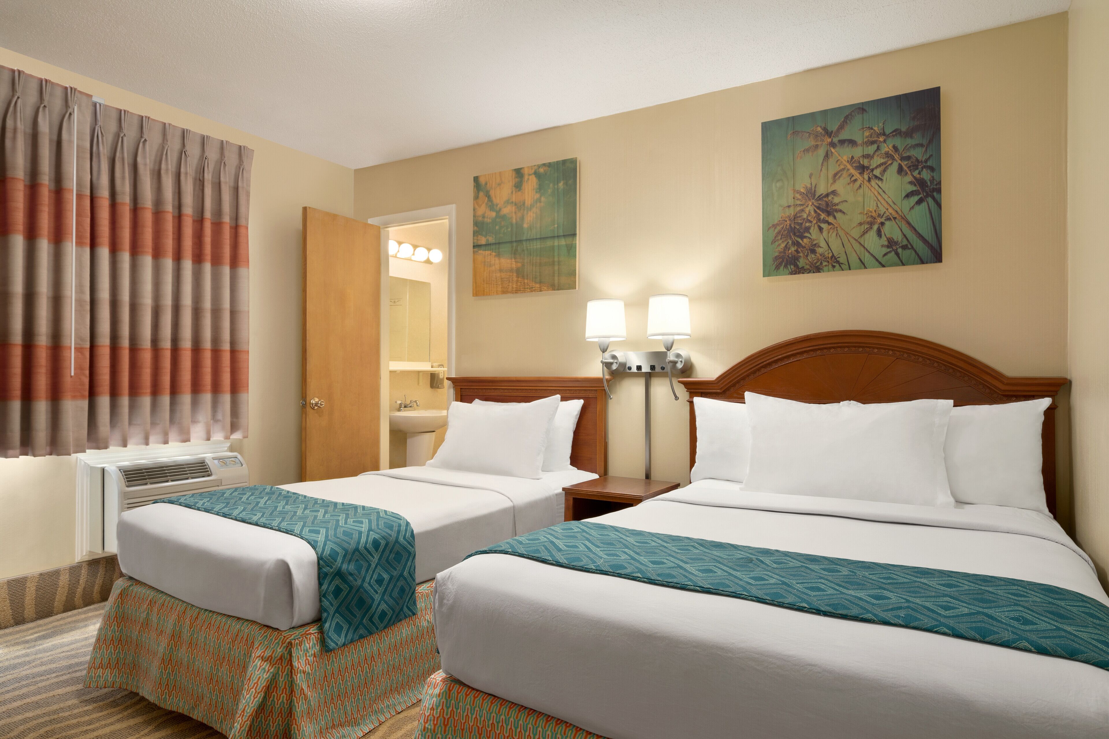 A hotel room with two beds, a bathroom, and a painting on the wall.
