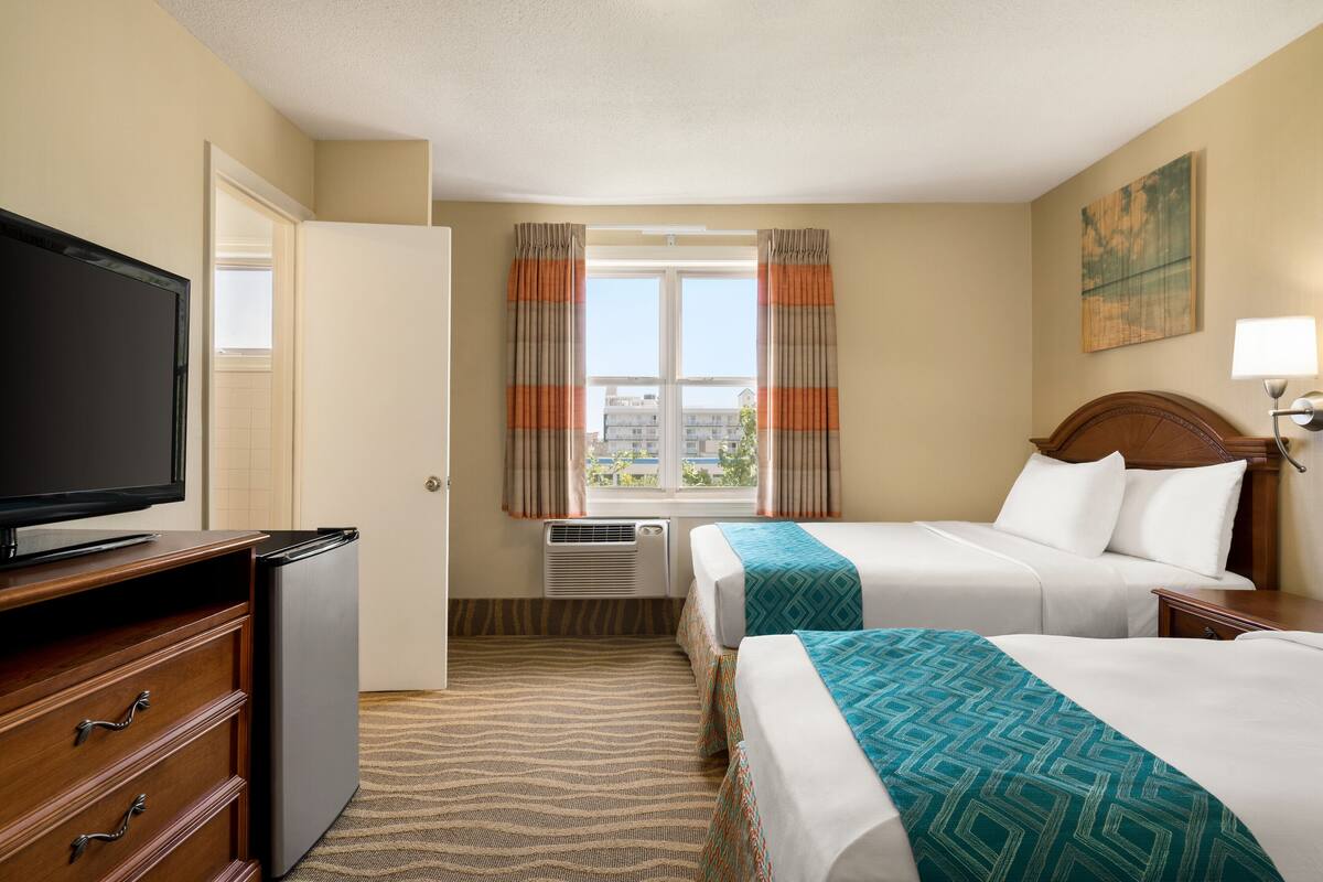 A hotel room with two beds, a TV, a dresser, and a window with curtains.