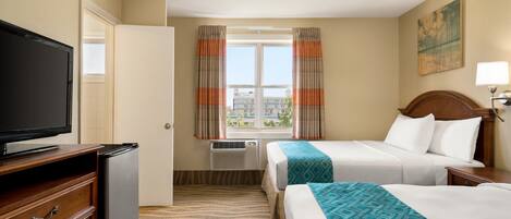 A hotel room with two beds, a TV, a dresser, and a window with curtains.