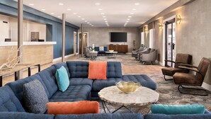 A spacious living area with a sectional sofa, a round coffee table, and a reception desk. - Plim Plaza Hotel (Ocean City)