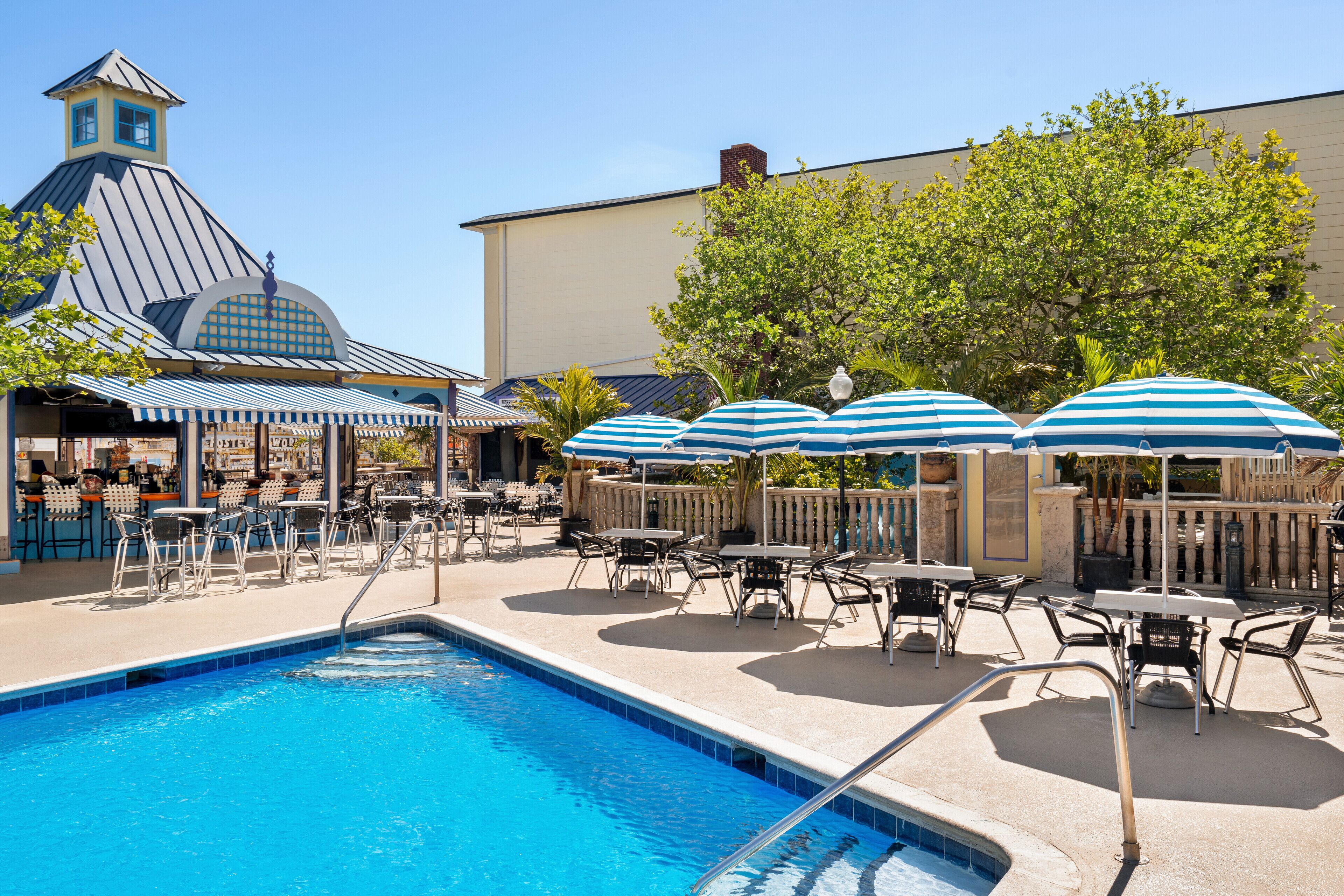 A pool area with lounge chairs and umbrellas, a bar, and a building with a distinctive tower.