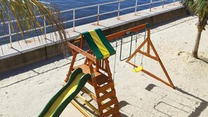 Une plage avec une aire de jeux, comprenant un toboggan et des balançoires, ainsi qu’un palmier.