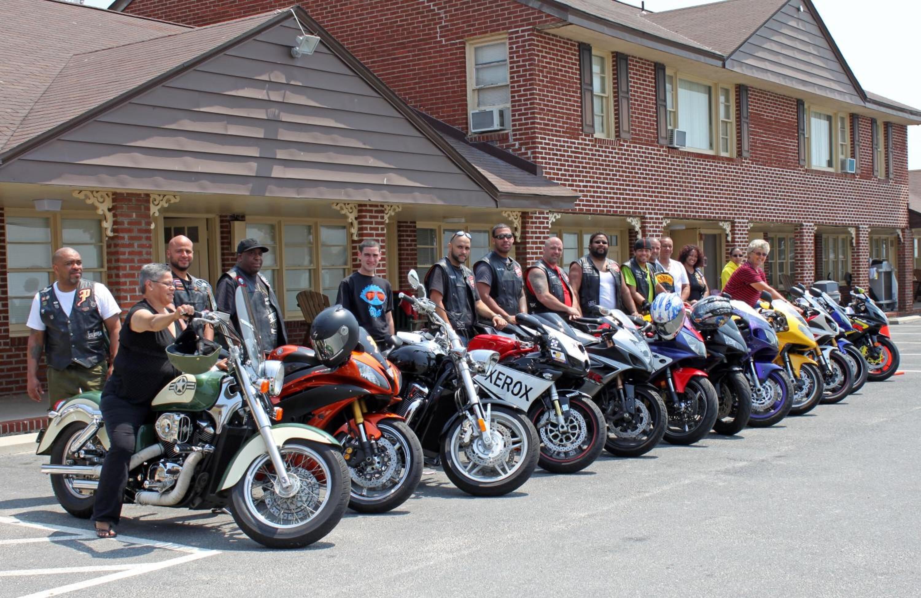A row of motorcycles parked in front of a building with a brick facade and a porch.