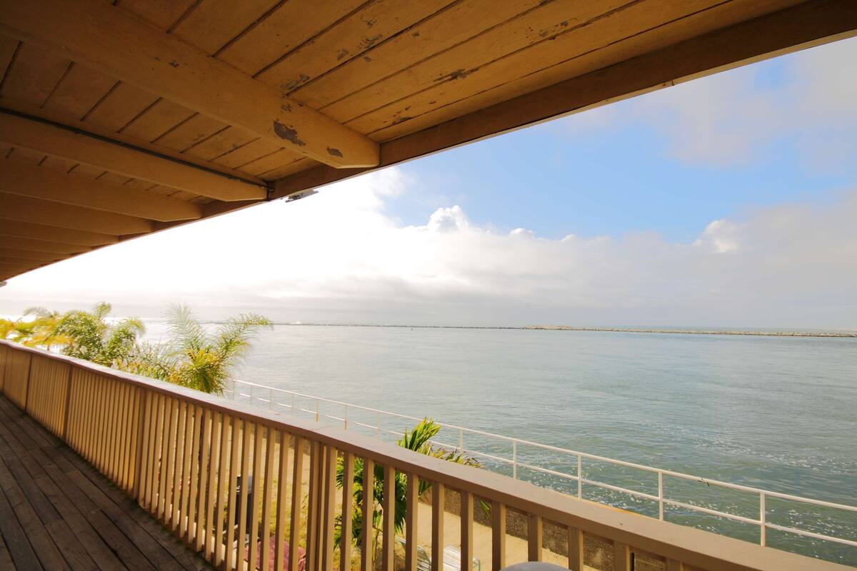 A wooden balcony overlooking a calm sea with a distant landmass and a clear sky.