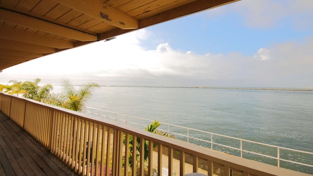 Un balcon en bois donnant sur une mer calme, avec une terre lointaine à l’horizon et un ciel dégagé.