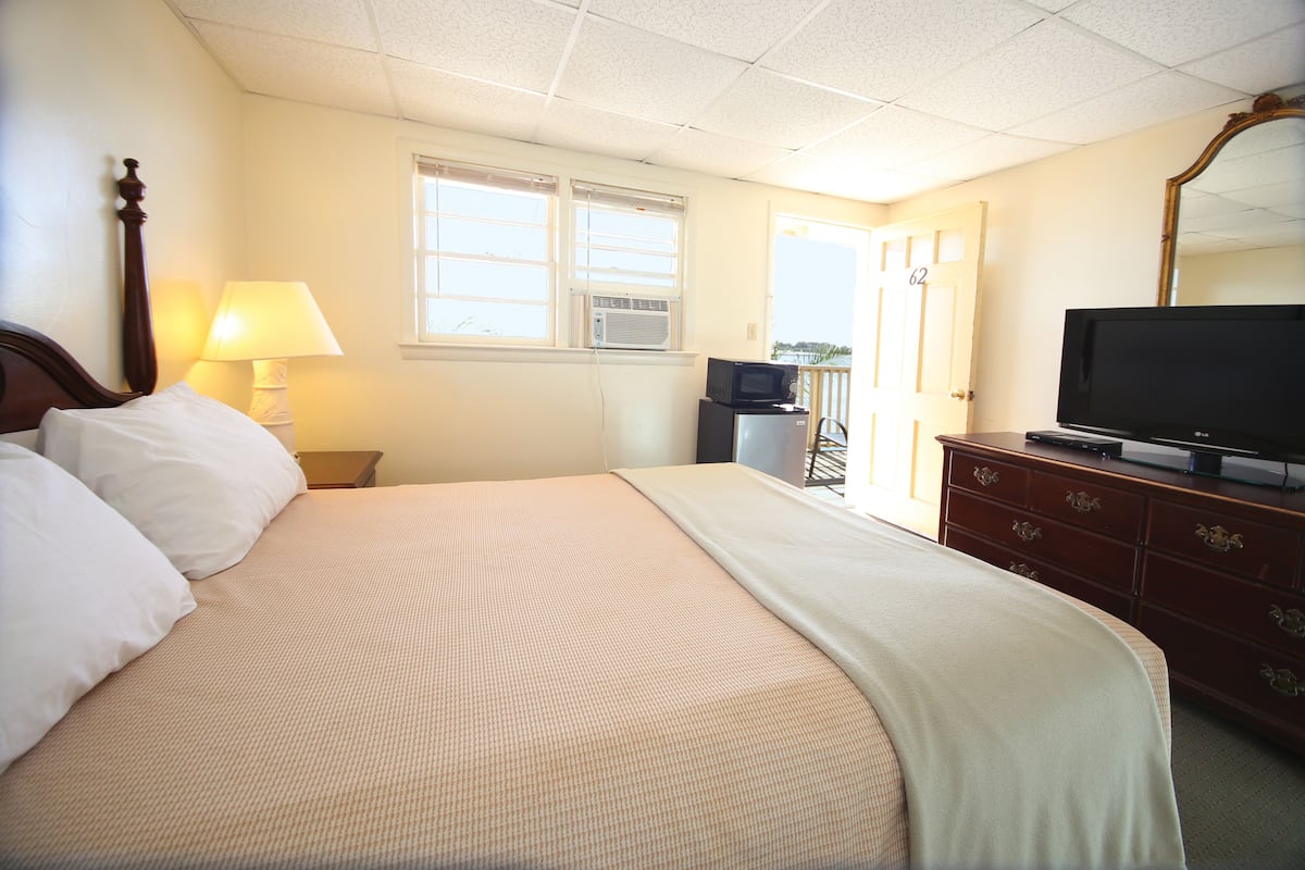 A hotel room with a large bed, a television, a dresser, and a window with blinds.