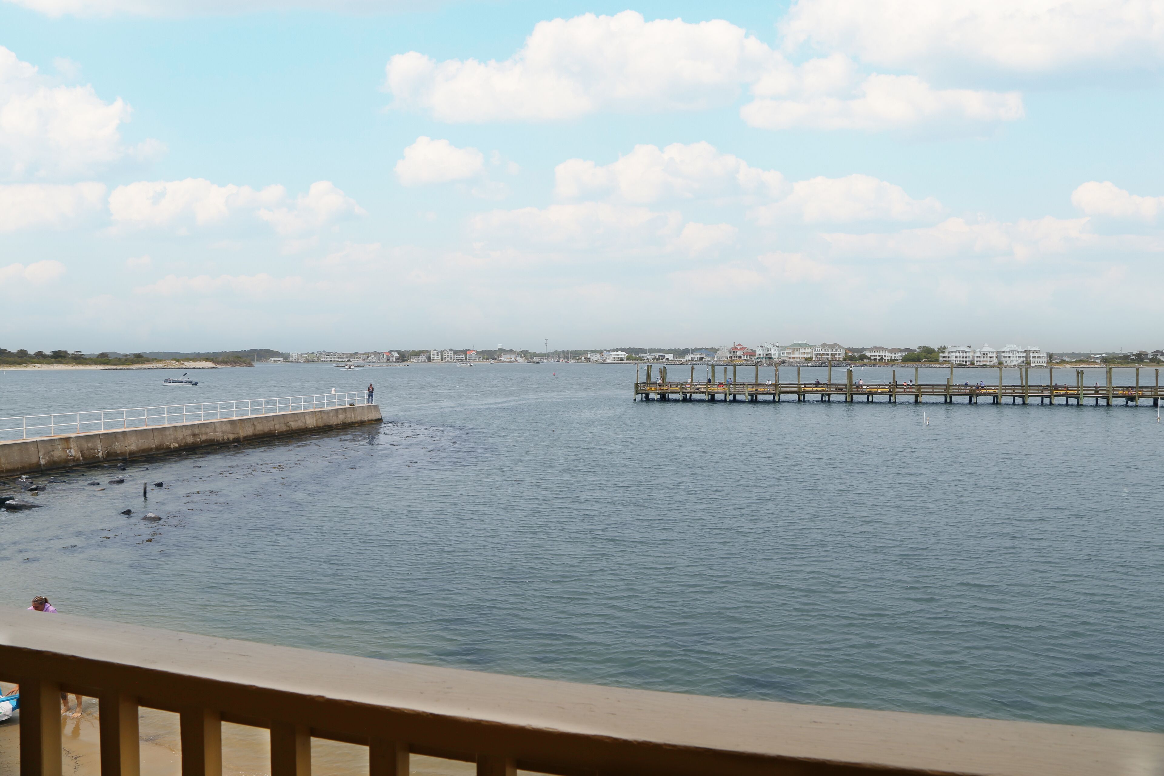 A waterfront view with a pier extending into the water, a sandy beach, and buildings in the background.