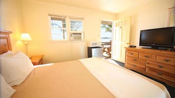 A hotel room with a bed, a television, a dresser, a lamp, and a window with an air conditioning unit.