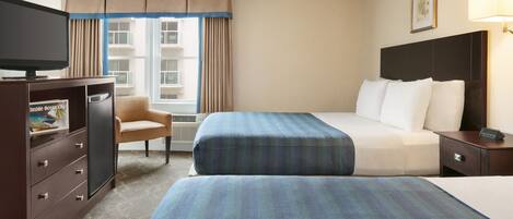 A hotel room with two beds, a TV, a desk, and a chair.