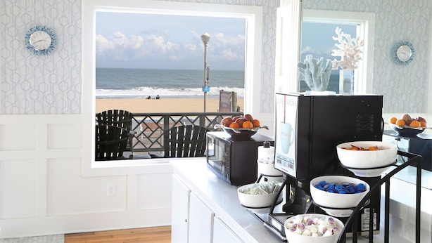 A kitchen with a view of the ocean, a dining area with chairs, and a buffet setup with various dishes. - Harrison Hall Hotel (Ocean City)