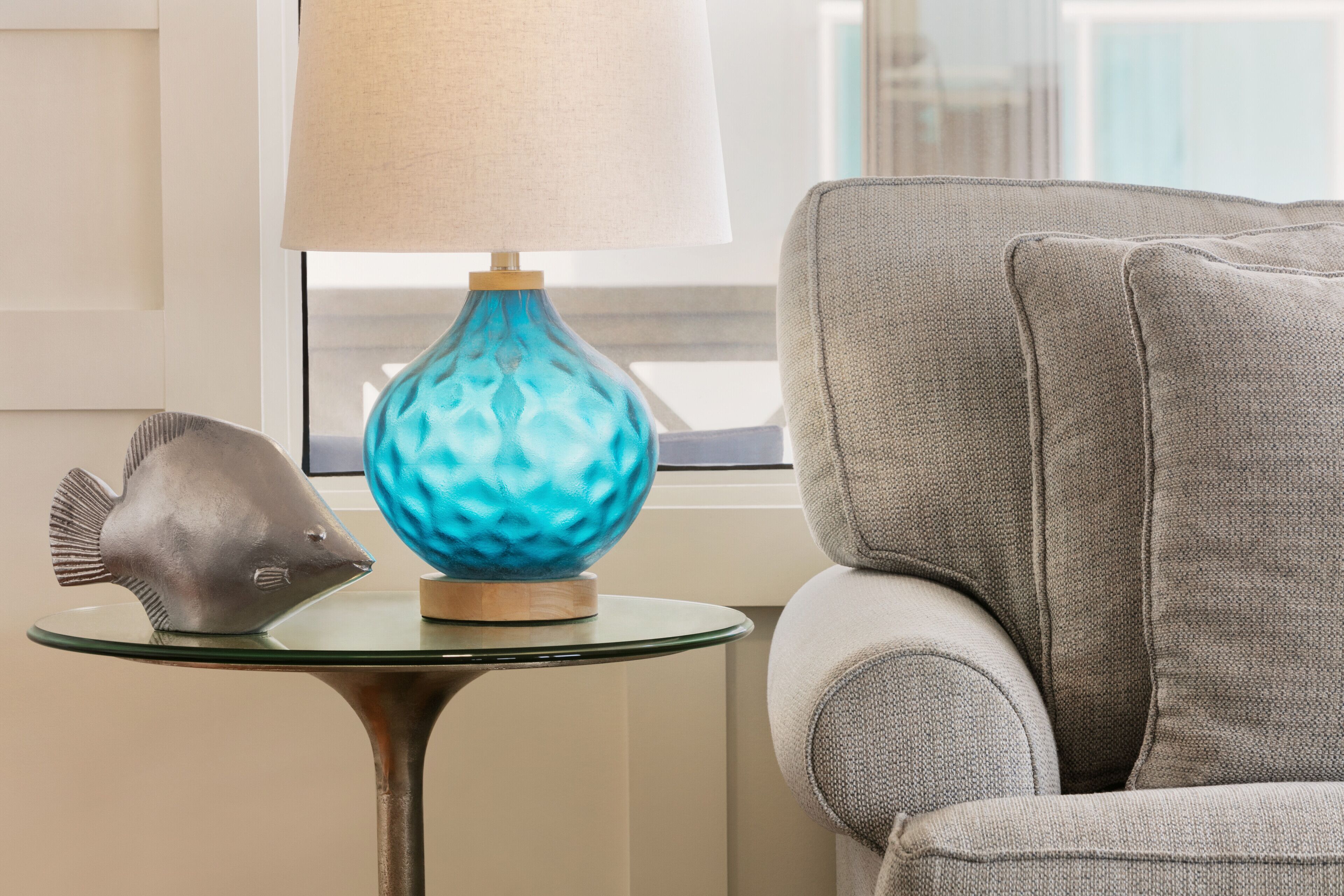 A modern living room with a grey sofa, a glass table, a blue decorative lamp, and a fish sculpture.