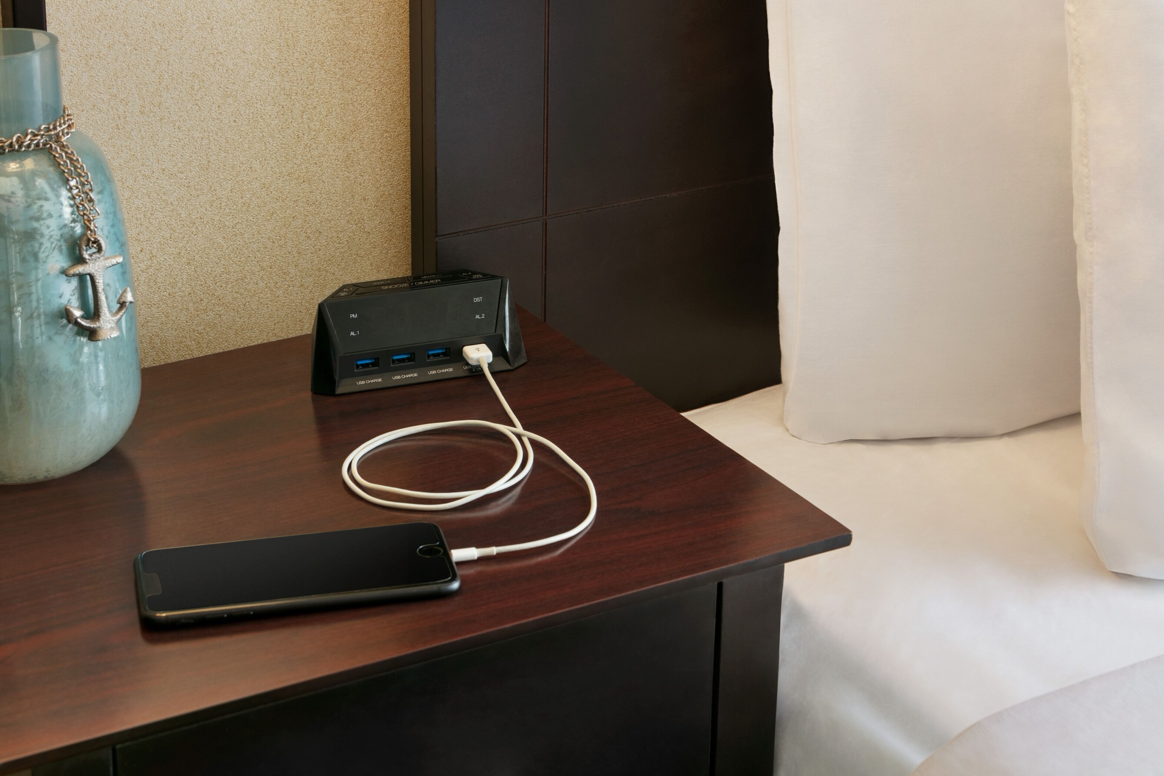 A smartphone connected to a charging dock on a wooden nightstand.