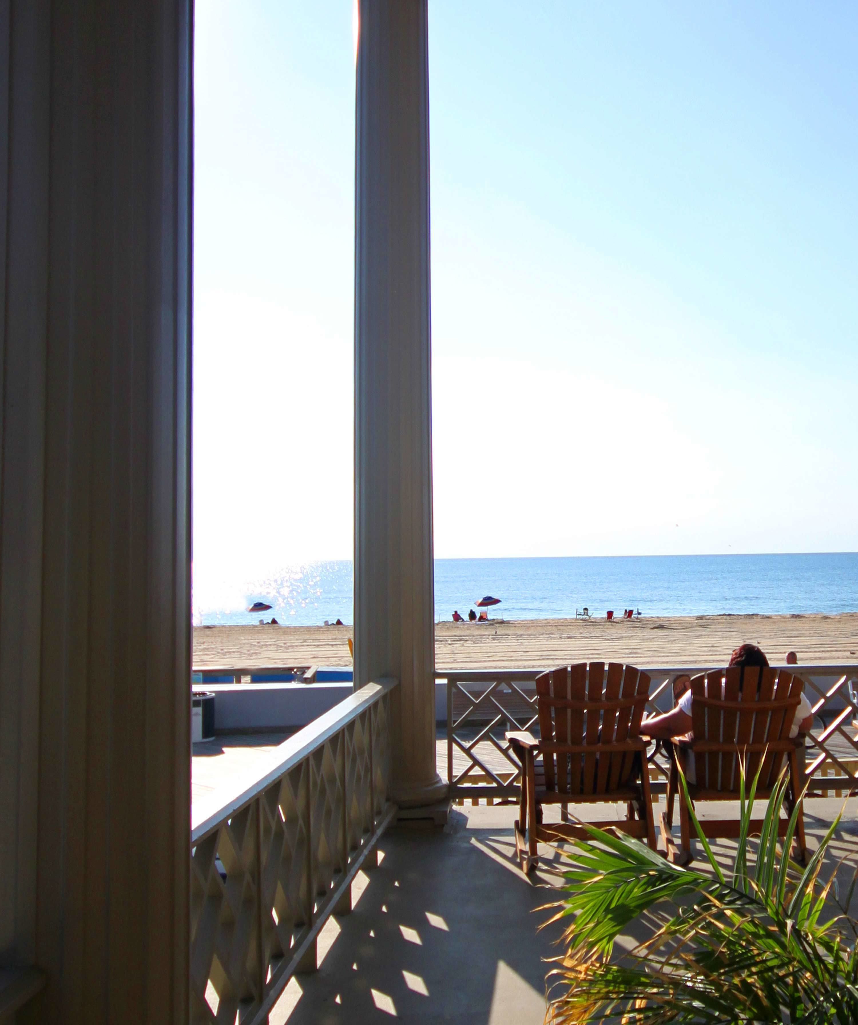 A beach view from a covered area with wooden chairs and a railing.