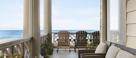 A balcony with wicker furniture, two Adirondack chairs, and potted plants.