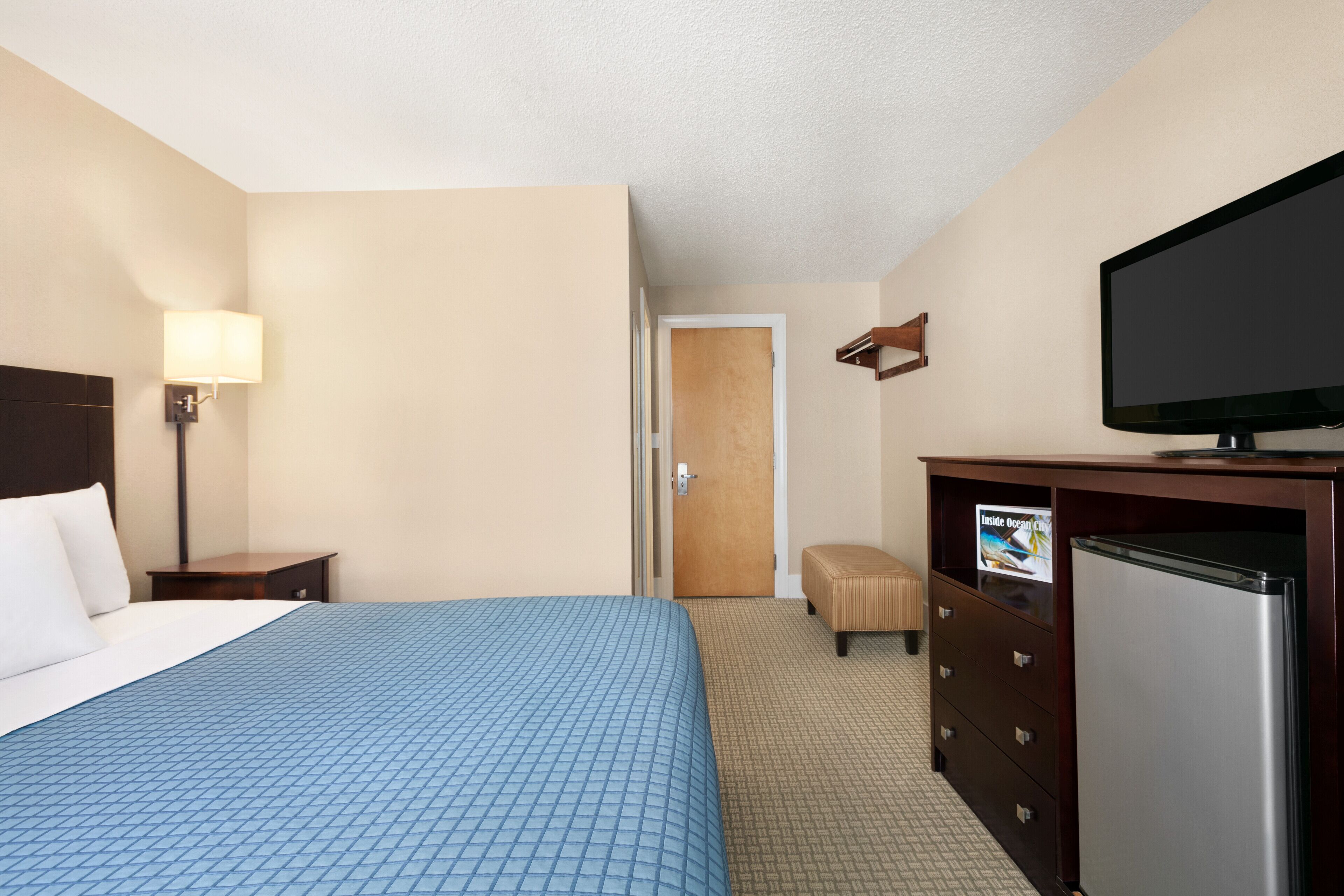Quarto de hotel com cama, televisão, frigorífico, secretária e candeeiro.