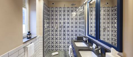 A modern bathroom with two sinks, a bathtub, and a shower area.
