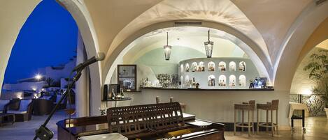 A grand piano in a well-lit, spacious room with arched ceilings and a bar area in the background.
