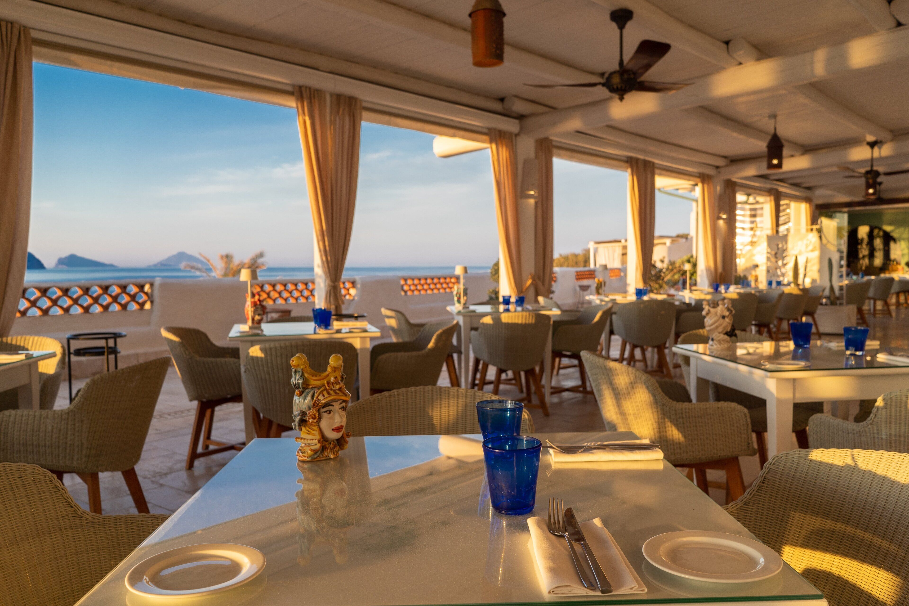 A restaurant with outdoor seating, tables, chairs, and a view of the sea.
